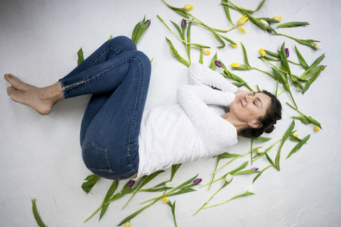 Lächelnde Frau auf dem Boden liegend inmitten von Tulpen, lizenzfreies Stockfoto