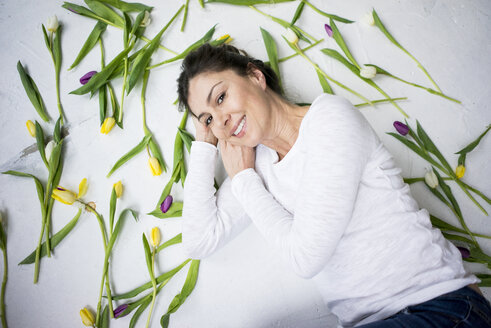 Smiling woman lying on floor amidst tulips - MOEF00813