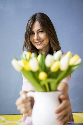 Portrait of smiling woman holding bunch of tulips in a jar stock photo