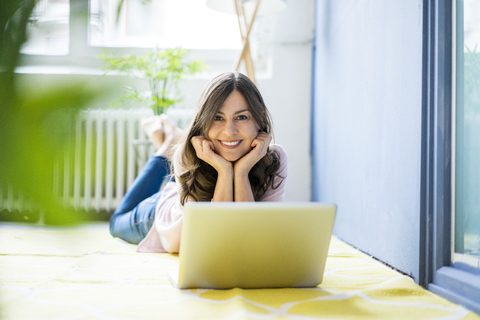 Portrait of smiling woman lying on floor with laptop stock photo