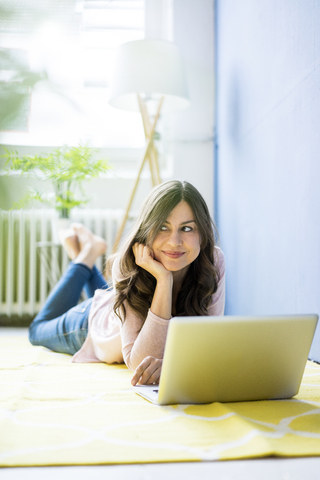 Lächelnde Frau auf dem Boden liegend mit Laptop, lizenzfreies Stockfoto