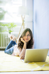 Smiling woman lying on floor with laptop - MOEF00824