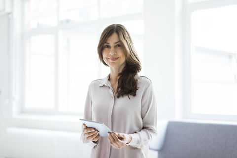 Portrait of smiling woman standing in bright room holding tablet stock photo