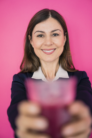Porträt einer lächelnden Geschäftsfrau vor einer rosa Wand, die ein Glas Saft hält, lizenzfreies Stockfoto