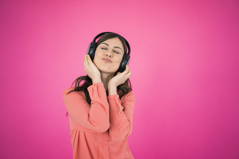 Frau vor rosafarbener Wand, die über Kopfhörer Musik hört, lizenzfreies Stockfoto