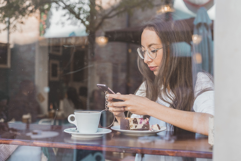 Frau mit Torte prüft ihr Handy in einem Café, lizenzfreies Stockfoto