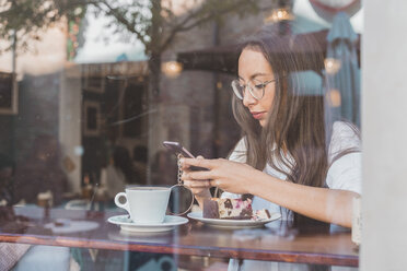 Frau mit Torte prüft ihr Handy in einem Café - AFVF00003