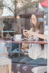 Frau mit Torte prüft ihr Handy in einem Café - AFVF00004