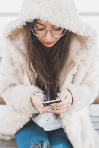 Stilvolle junge Frau sitzt auf einer Bank und benutzt ein Mobiltelefon, lizenzfreies Stockfoto