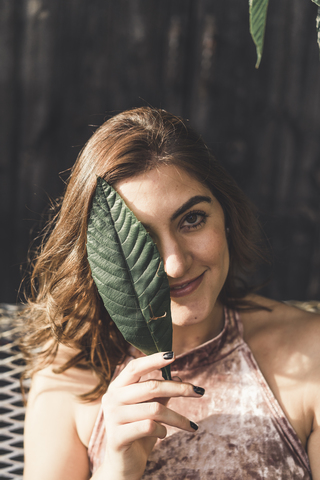 Portrait of smiling young woman covering eye with a leaf stock photo