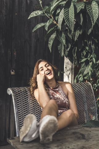 Porträt einer lachenden jungen Frau, die auf einer Bank im Freien sitzt, lizenzfreies Stockfoto