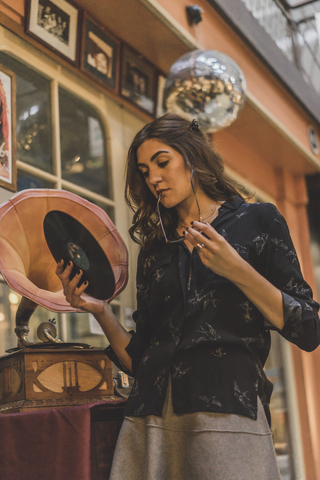Portrait of pensive young woman standing in front of antique shop holding gramophone record stock photo