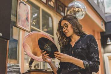 Porträt einer lächelnden jungen Frau, die vor einem Antiquitätengeschäft steht und eine Grammophonplatte betrachtet - AFVF00053