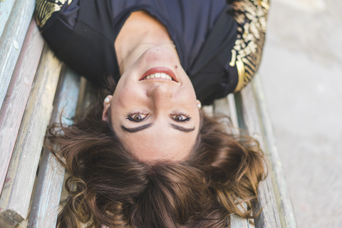 Portrait of laughing young woman lying on a bench stock photo