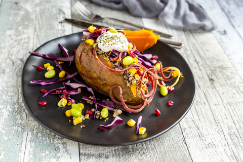 Kumpir, gefüllte Süßkartoffel, Rotkohl, Mais, Edamame, Karotten, Quinoa, Crème fraîche auf Teller, lizenzfreies Stockfoto