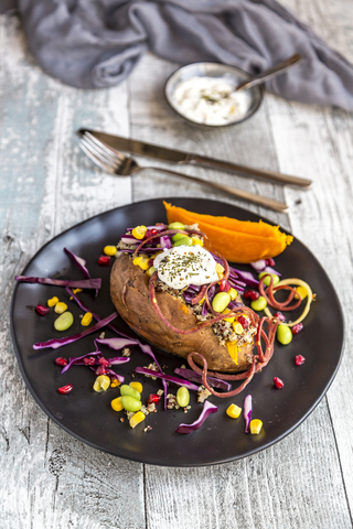 Kumpir, gefüllte Süßkartoffel, Rotkohl, Mais, Edamame, Karotten, Quinoa, Crème fraîche auf Teller, lizenzfreies Stockfoto