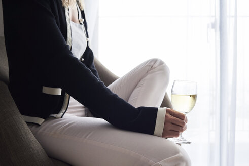 Nahaufnahme einer Frau, die zu Hause im Sessel sitzend ein Glas Wein trinkt - IGGF00403