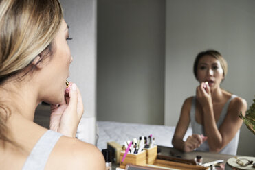 Woman at home using makeup applying lipstick in front of a mirror - IGGF00410