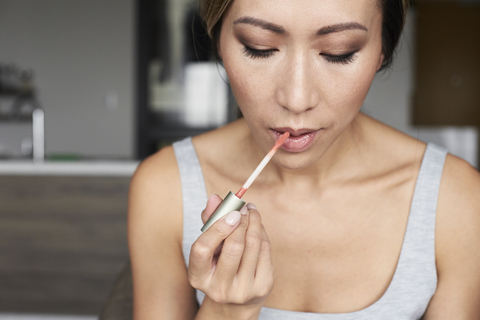 Woman at home using makeup applying lip gloss stock photo