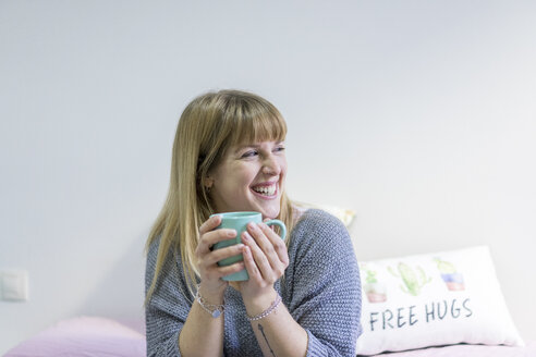 Porträt einer lachenden jungen Frau mit Kaffeetasse zu Hause - AFVF00068