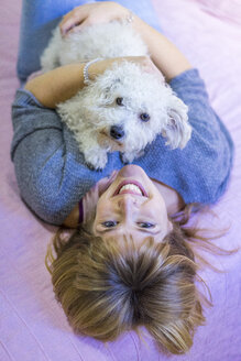 Porträt einer glücklichen Frau auf dem Bett liegend mit ihrem Hund - AFVF00072