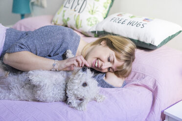 Happy woman lying on bed with her dog - AFVF00073