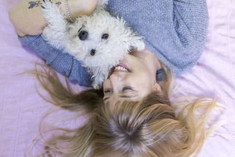 Happy woman lying on bed with her dog stock photo