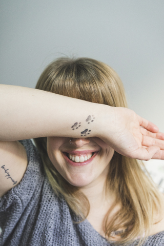 Lachende tätowierte Frau, die ihre Augen mit dem Arm bedeckt, lizenzfreies Stockfoto