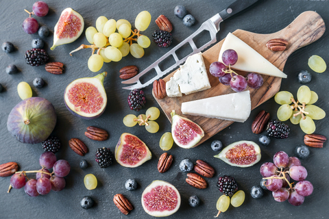 Plate with cheese, figs, grapes, blueberries, brambles, pecan nuts, chopping board, knife stock photo