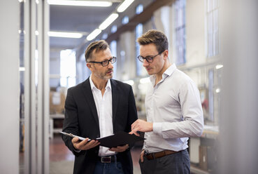 Two businessmen in factory looking at folder - DIGF03329