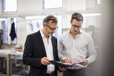 Two businessmen in factory looking at folder - DIGF03330