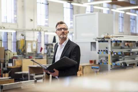 Mature businessman in factory holding folder stock photo