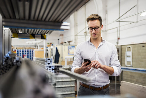 Junger Geschäftsmann benutzt Mobiltelefon in einer Fabrik - DIGF03346