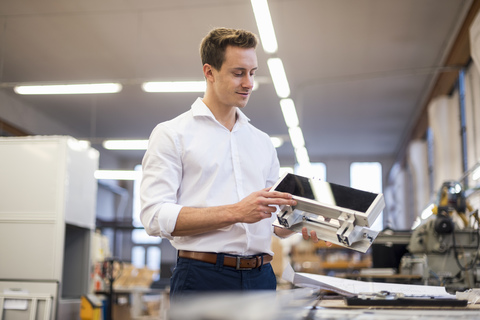 Smiling young businessman in factory holding component stock photo