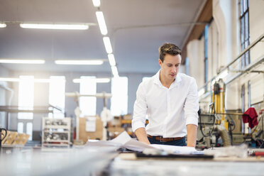 Junger Geschäftsmann arbeitet in einer Fabrik an einem Plan - DIGF03364