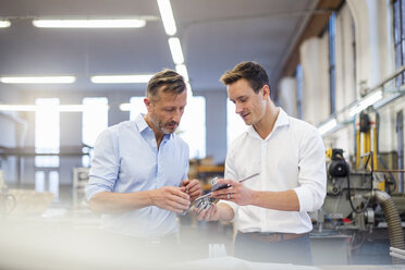 Two businessmen in factory discussing product - DIGF03368