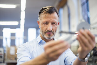 Reifer Geschäftsmann in Fabrik, der ein Bauteil untersucht - DIGF03369