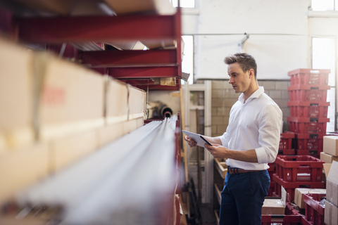 Young businessman in factory storeroom using tablet stock photo