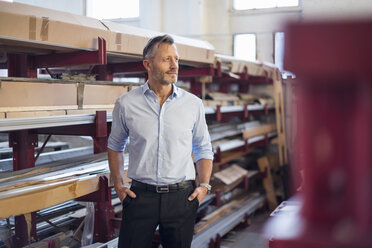 Mature businessman standing in factory storeroom looking sideways - DIGF03372