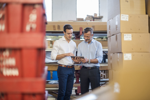 Two businessmen in factory storeroom looking at tablet stock photo