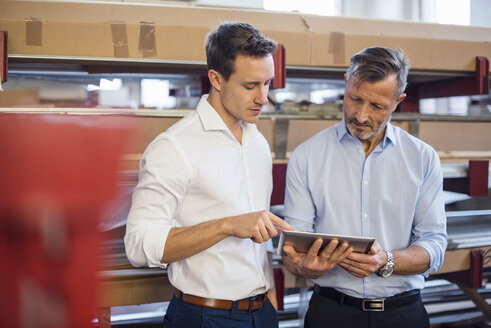 Zwei Geschäftsleute im Lagerraum einer Fabrik, die ein Tablet betrachten - DIGF03375