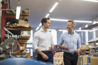 Two businessmen walking and talking in factory storeroom - DIGF03376