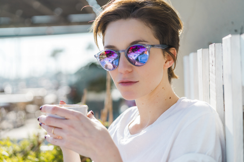 Portrait of woman with cup of coffee wearing mirrored sunglasses stock photo