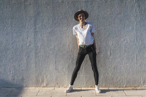 Laughing woman wearing hat standing in front of tiled wall at sunlight stock photo