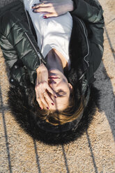 Porträt einer Frau mit Kapuzenjacke auf dem Boden liegend im Sonnenlicht - AFVF00110