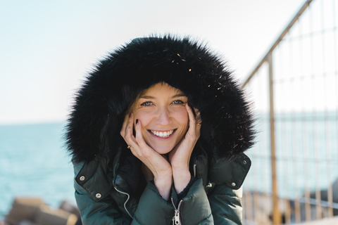 Porträt einer glücklichen Frau mit Kopf in den Händen und Kapuzenjacke, lizenzfreies Stockfoto