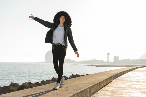 Spanien, Barcelona, Frau mit Kapuzenjacke balanciert auf Promenade, lizenzfreies Stockfoto