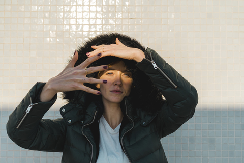 Portrait of woman wearing hooded jacket in front of tiled wall stock photo