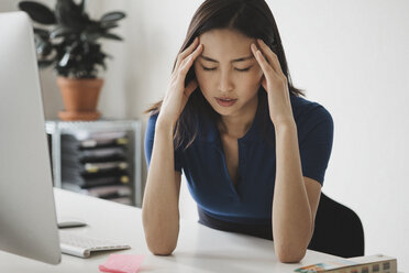 Junge Geschäftsfrau mit Kopfschmerzen am Schreibtisch im Büro - FSIF01376