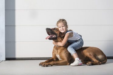 Porträt eines süßen Mädchens auf einem Hund sitzend im Freien - FSIF01389